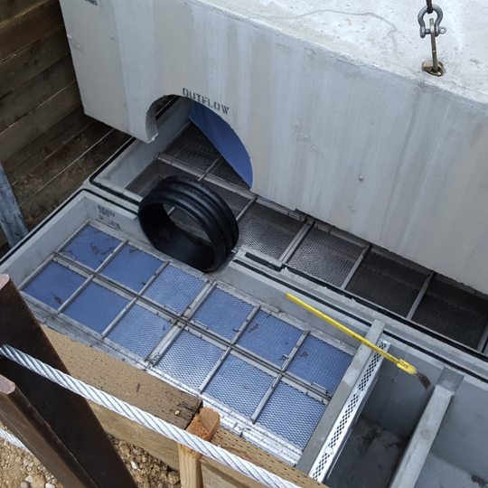 Concrete stormwater treatment chamber with filtration grates and pipes installed at a construction site.
