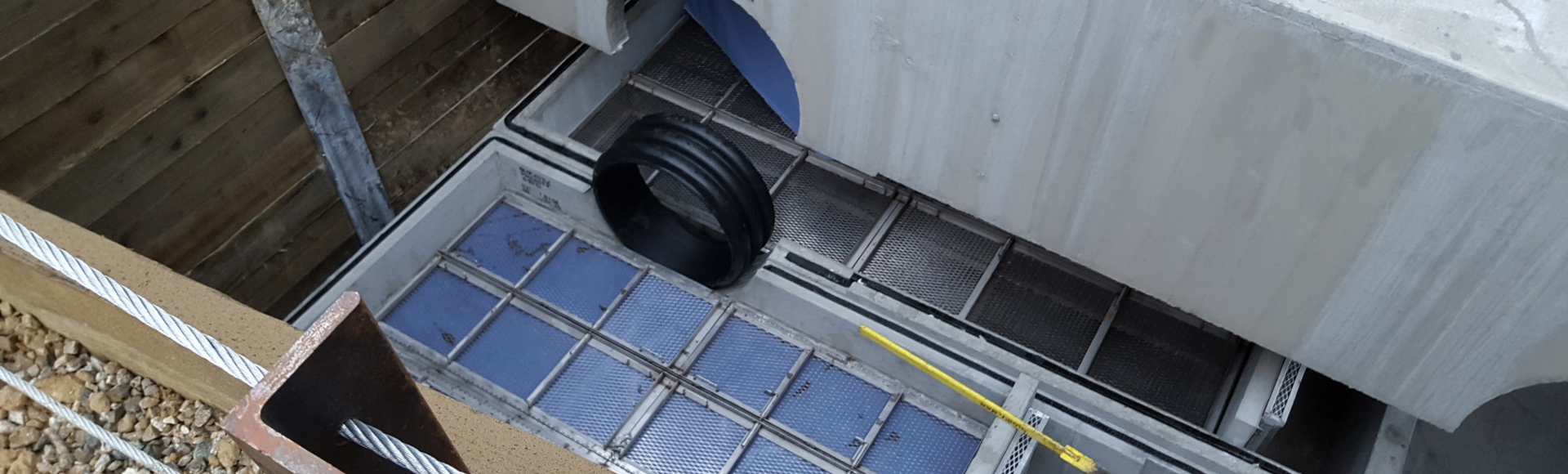 Concrete stormwater treatment unit with metal grates and plastic pipes installed at a construction site.
