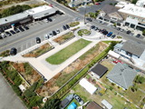 Rectangular rain garden with ornamental grasses, shrubs, and mulch, bordered by concrete and surrounded by young plants.